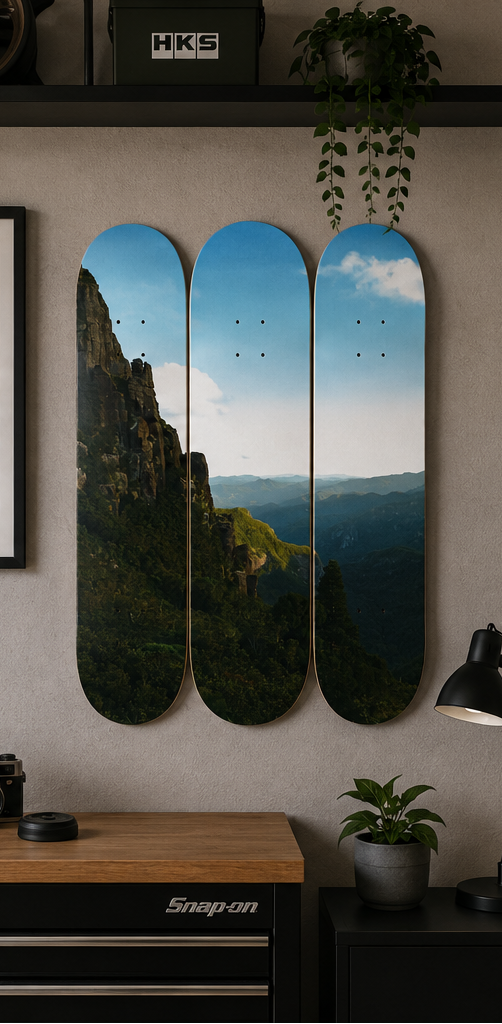 Set of skateboard decks with mountain landscape design on a white background, displayed on a wall.