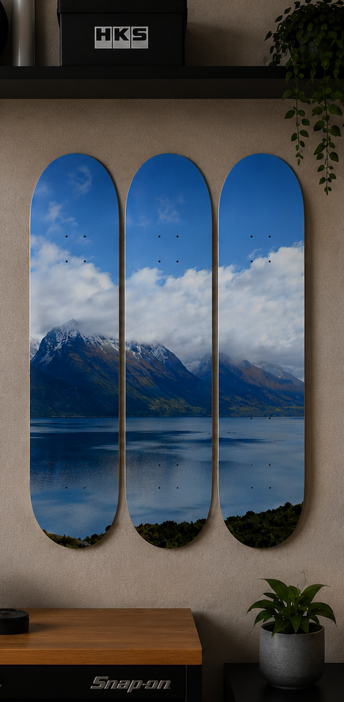 Three skateboard decks with a mountain and lake scene, displayed on a wall.